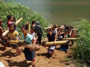 The boat is tied up and the students and teachers carry the banana trees up the sandy bank to a pile.